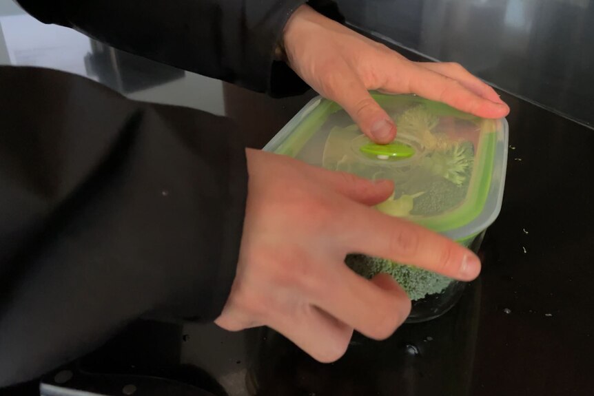 Two hands close the lid of a plastic container with broccoli inside .