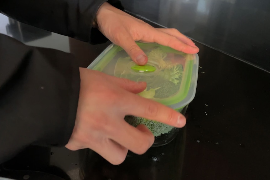 Two hands shut the lid on a plastic container with broccoli inside.
