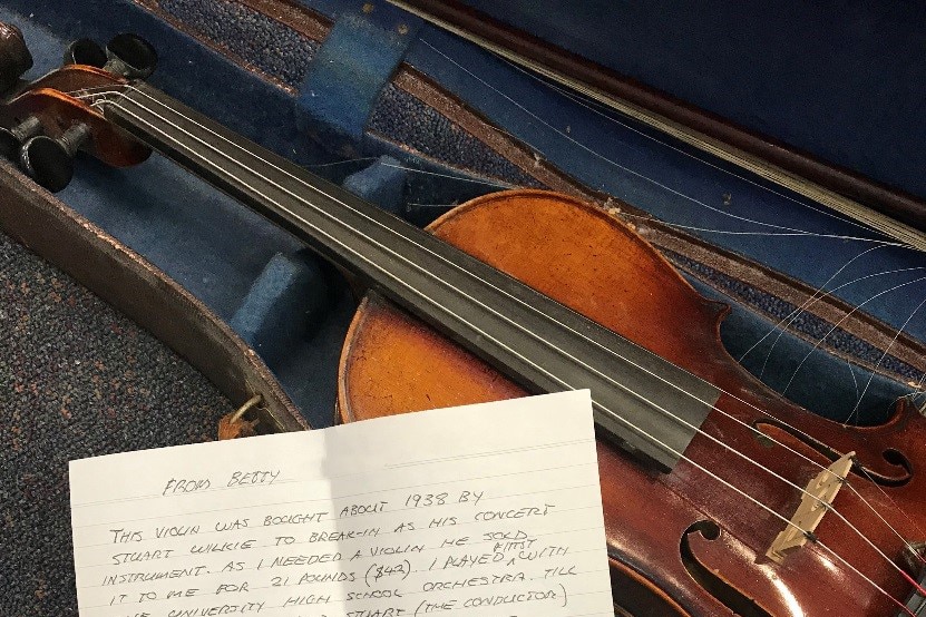 A violin lies in an open case with a handwritten letter on top.