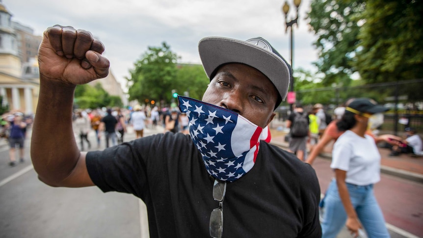 A man with an American flag bandana on his mouth with his fist in the air