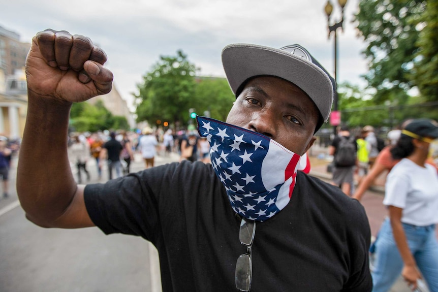 A man with an American flag bandana on his mouth with his fist in the air