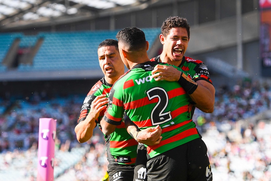 Three South Sydney NRL players embrace as they celebrate a try scored against the Newcastle Knights.