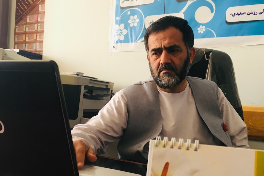 A man with a beard sits at a computer desk.