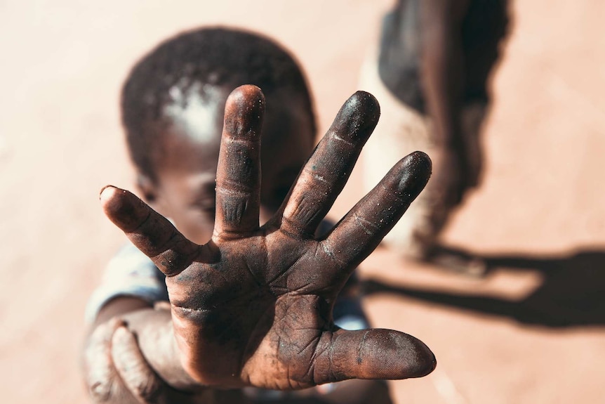A young boy in Africa puts his hand up to the camera, covering his face from view.