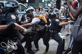 Anti-police violence protesters clash with police officers in the streets of New York. Their expressions are pained.