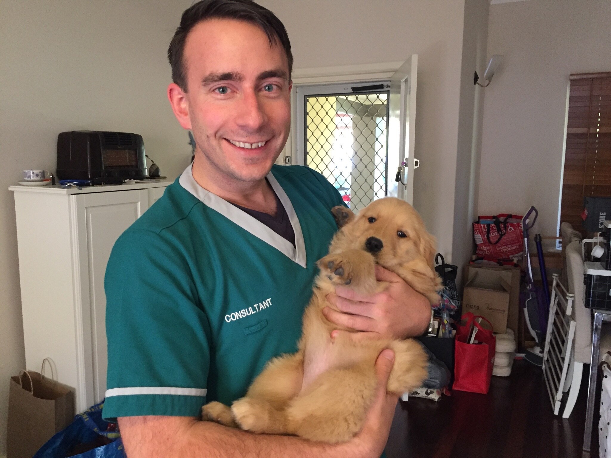 Man in scrubs holding a dog.