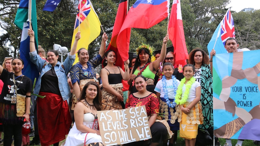 A group of pacific islander women hold flags from pacific island nations.