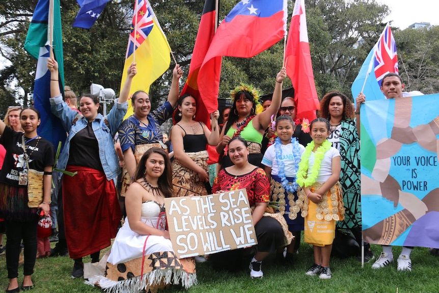 A group of pacific islander women hold flags from pacific island nations.