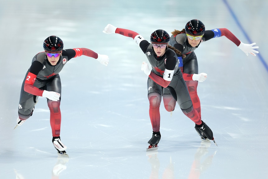Three fe,male Dutch speed skaters race down the icy straight to the finish with arms flailing during a pursuit event.