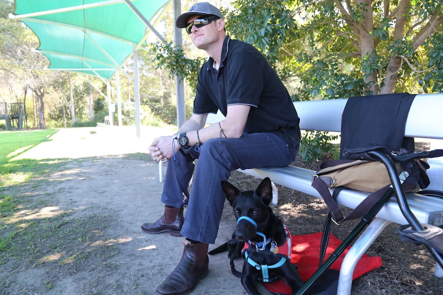 Ed Bennett sits on a bench with his service dog at his feet.