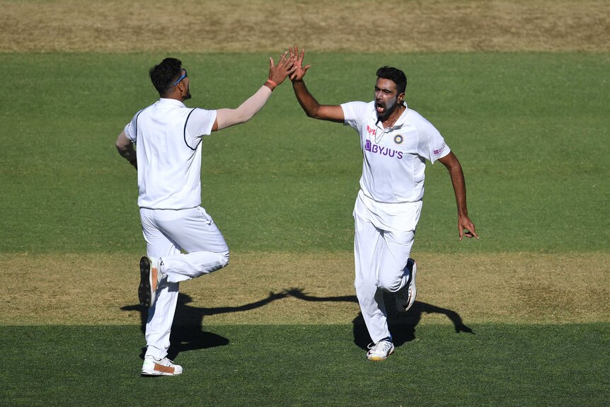Ravi Ashwin runs with his mouth open and arm up, high-fiving a teammate