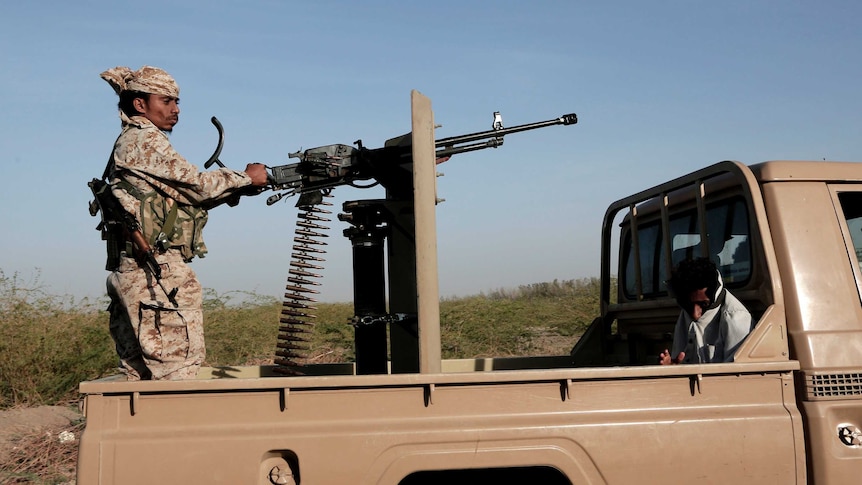 A soldier stands on the back of a ute.