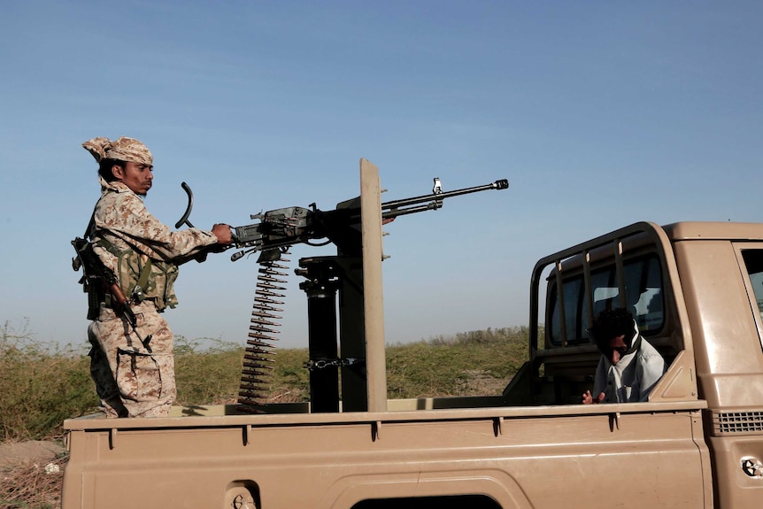 A soldier stands on the back of a ute.