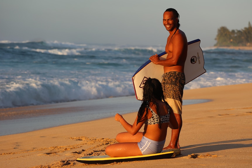 A man with a bodyboard stands next to his daughter.