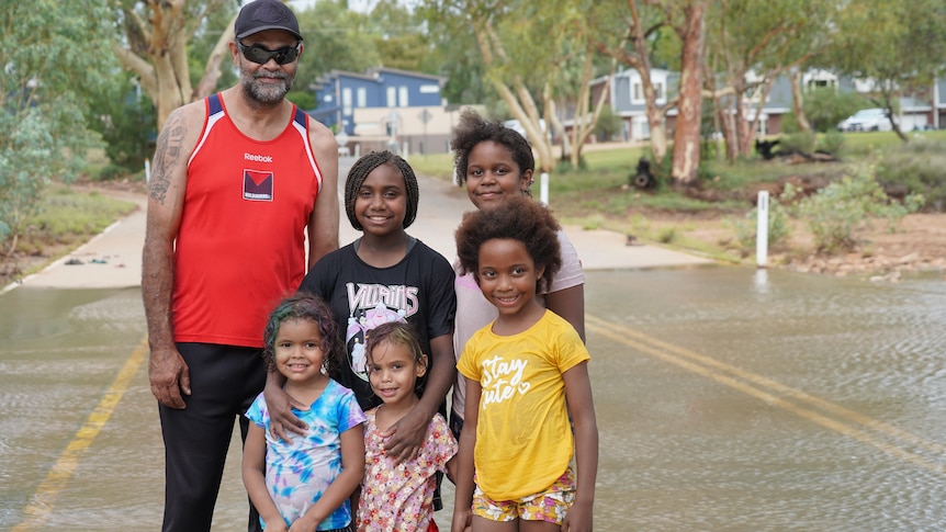 A man a his five daughters stand in a flooded river. 