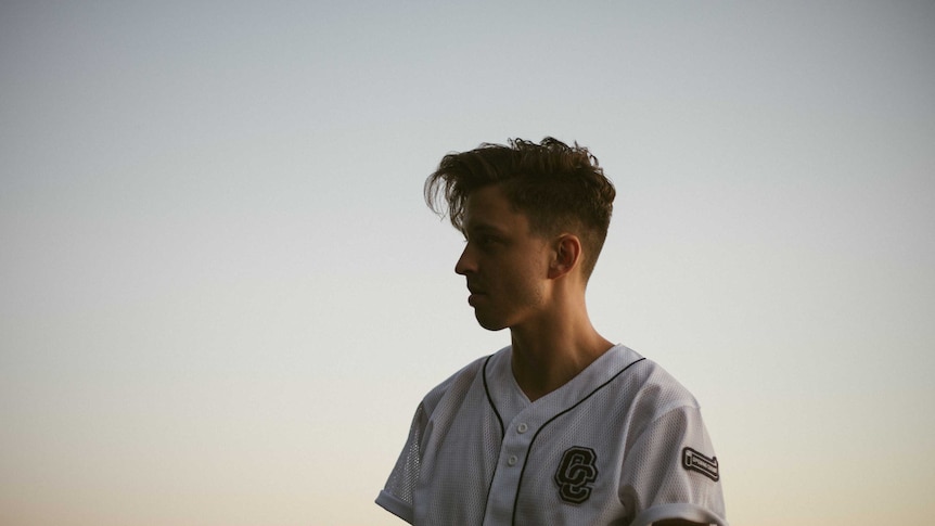 Ekali standing outside with the sunset behind him, looking away from the camera wearing a softball jersey