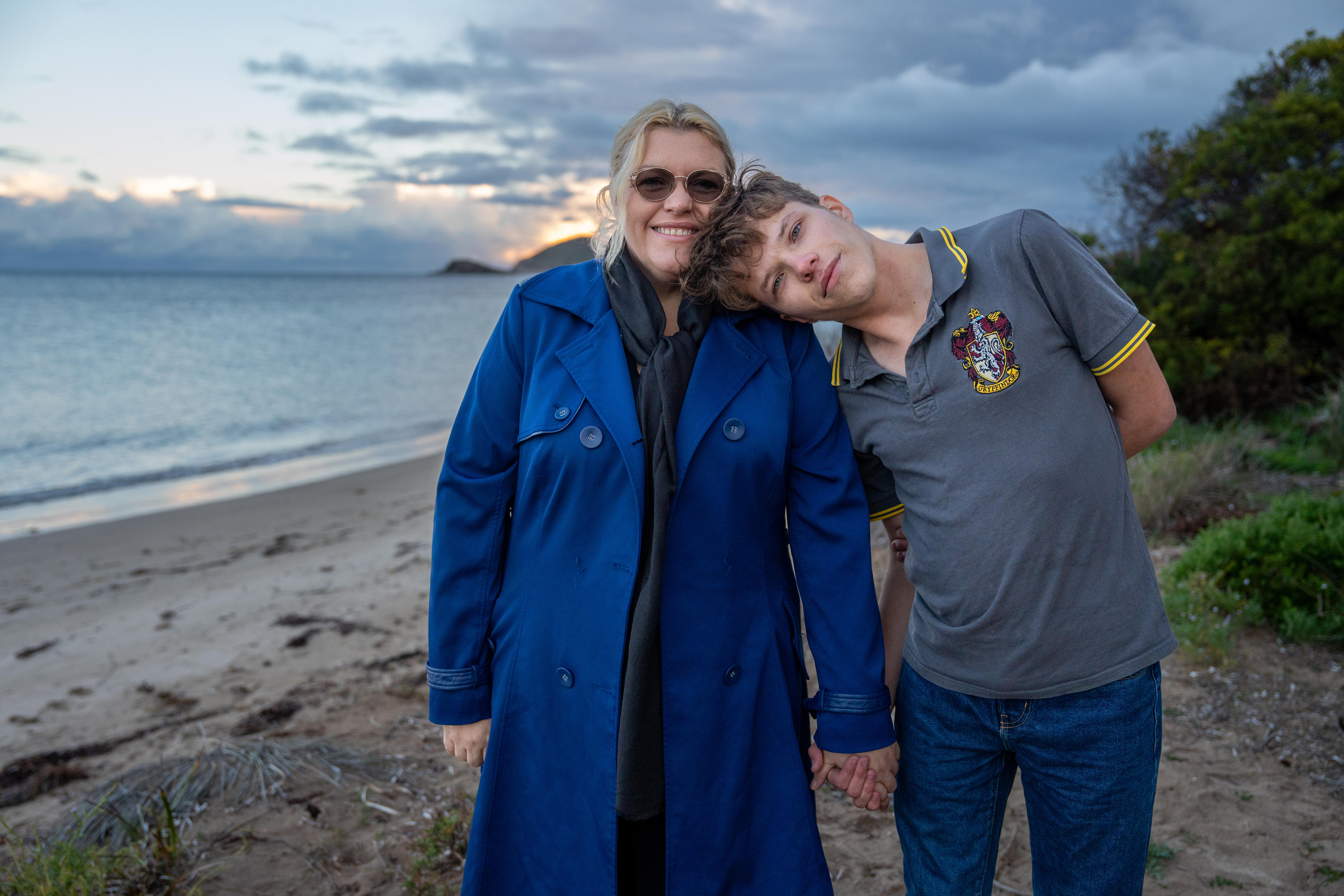 A son leans on his mother's shoulder in front of an ocean