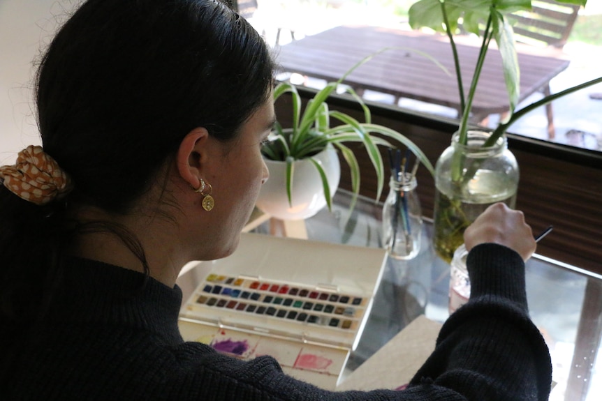 A dark-haired woman at work on a small painting.