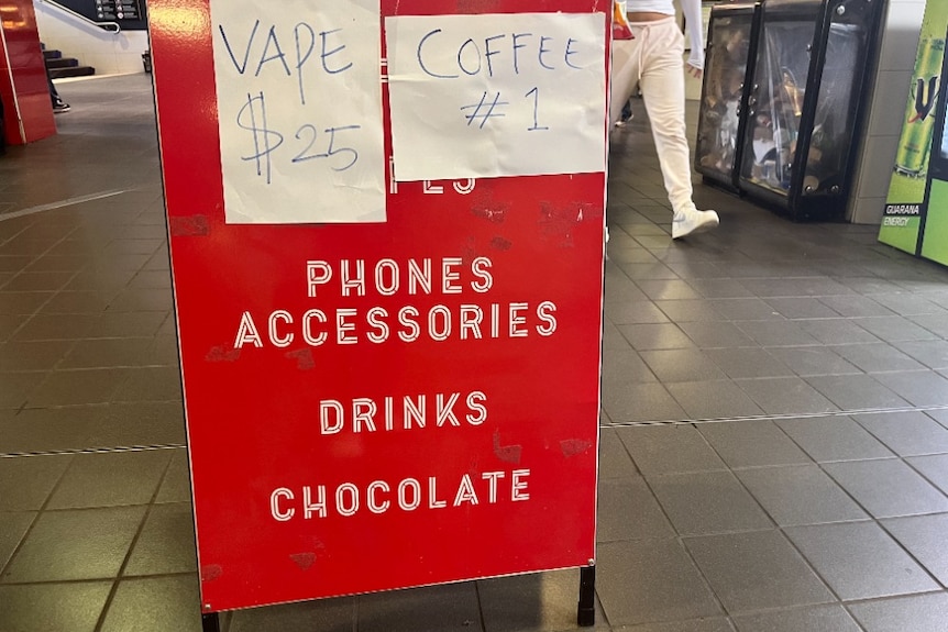 A red sandwich board advertises Vapes for $25 alongside other items