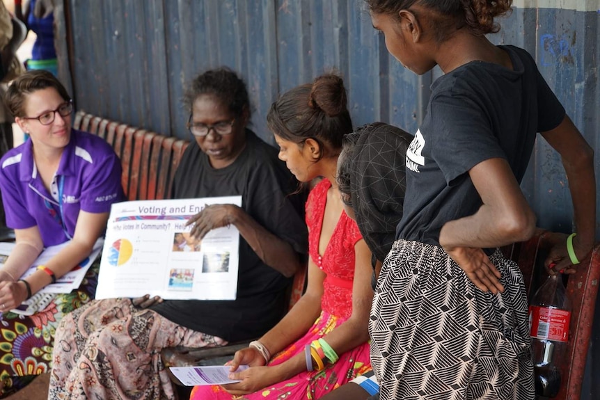 Women gather around to read an enrolment guide.