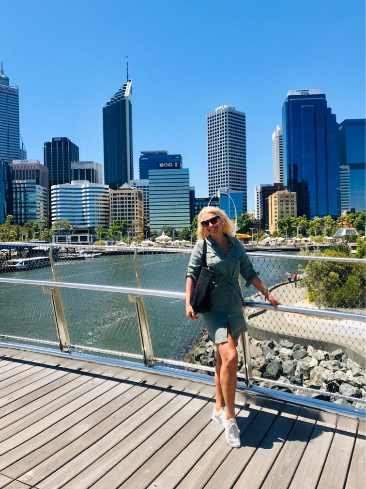 A woman stands on a bridge over a river. There's tall city buildings in the background.