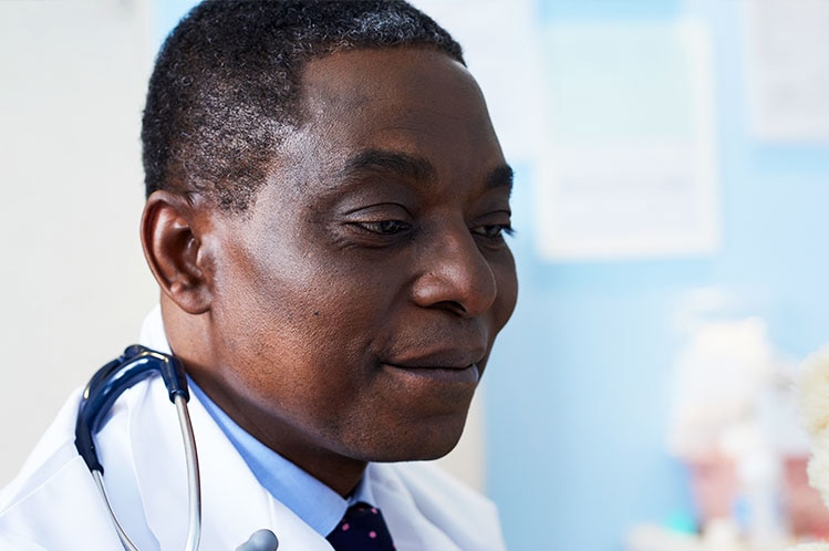 Dr George Ofori-Amanfo wearing a blue collared shirt, tie and lab coat, with a stethoscope draped over his shoulder.