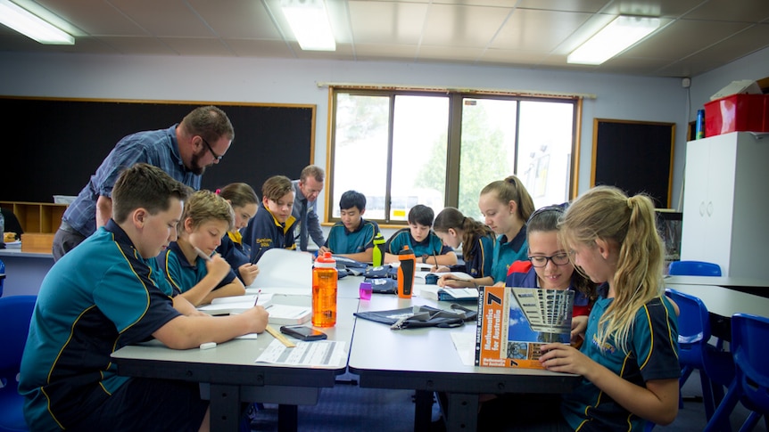 Man stands over a group of children who are learning at a desk