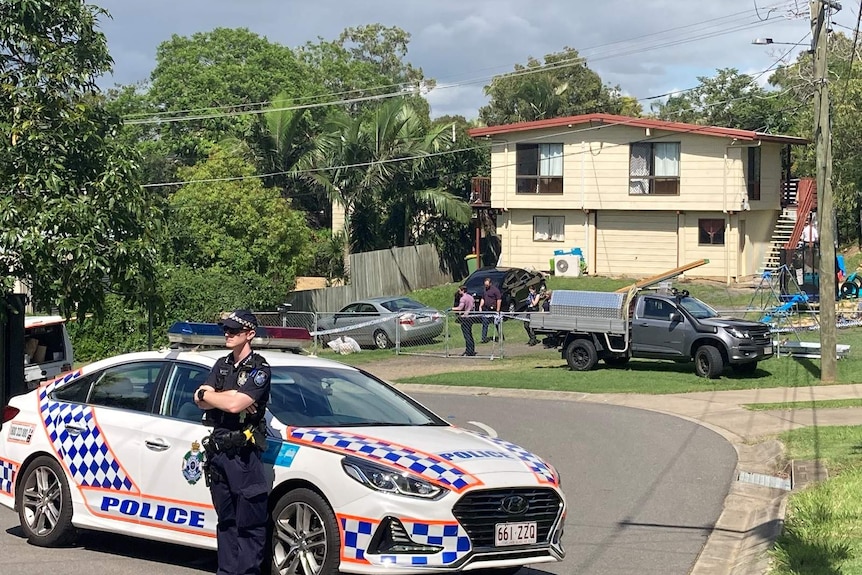 A policeman in front of a police car guarding a house that has been declared a crime scene