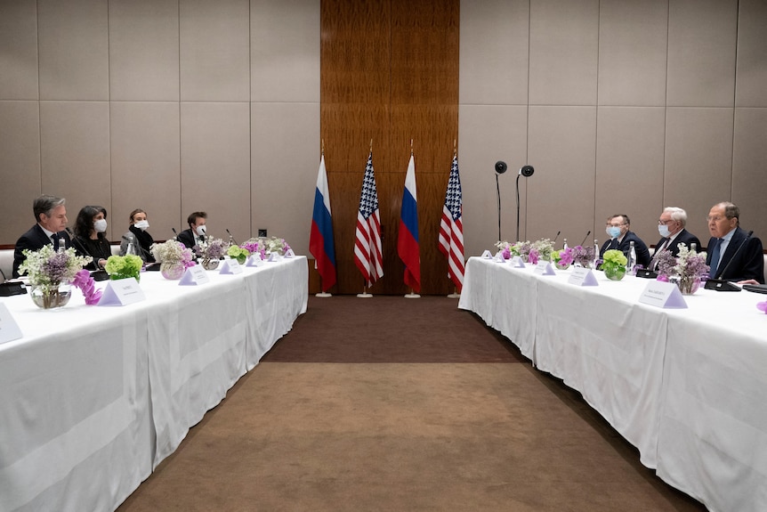 The Leaders Are Seated At Long Tables And Facing Each Other With Us And Russian Flags In The Background.