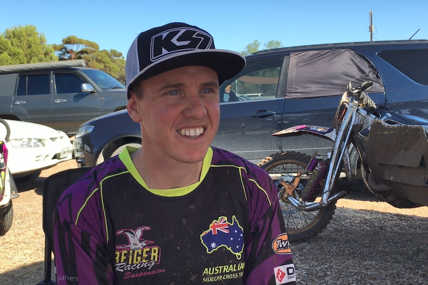 A young man in motorcycle gear and a black and white cap.