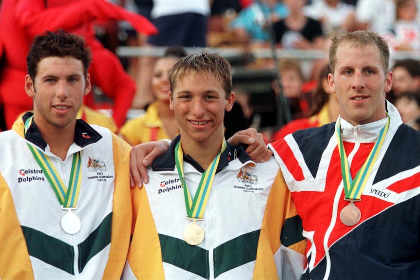 A young Australian swimmer with a gold medal stands beside two other medallists at a world titles.