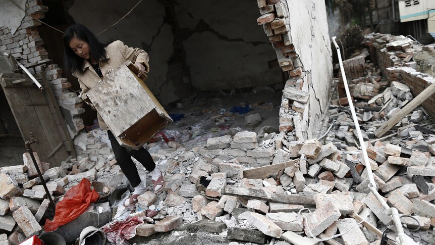 A resident carries furniture out of her damaged house after Saturday's China earthquake.