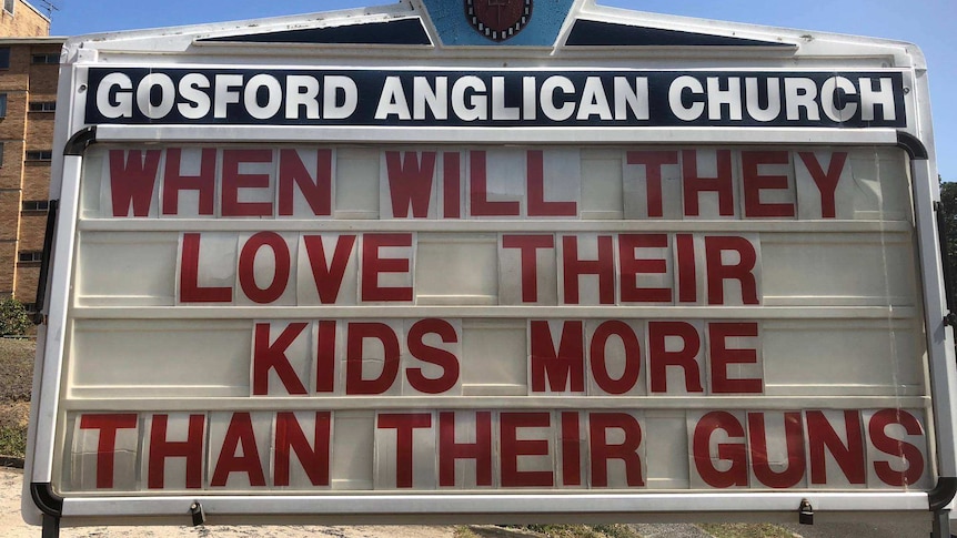 A sign reads, "When will they love their kids more than their guns".
