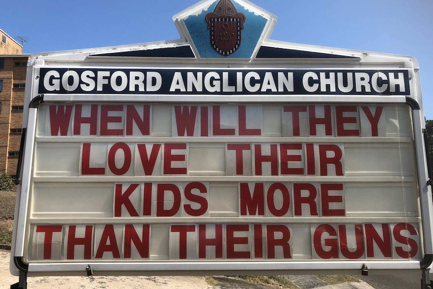 A sign reads, "When will they love their kids more than their guns".