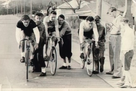 A vintage black and white photograph of cyclists as a few spectators watch on.