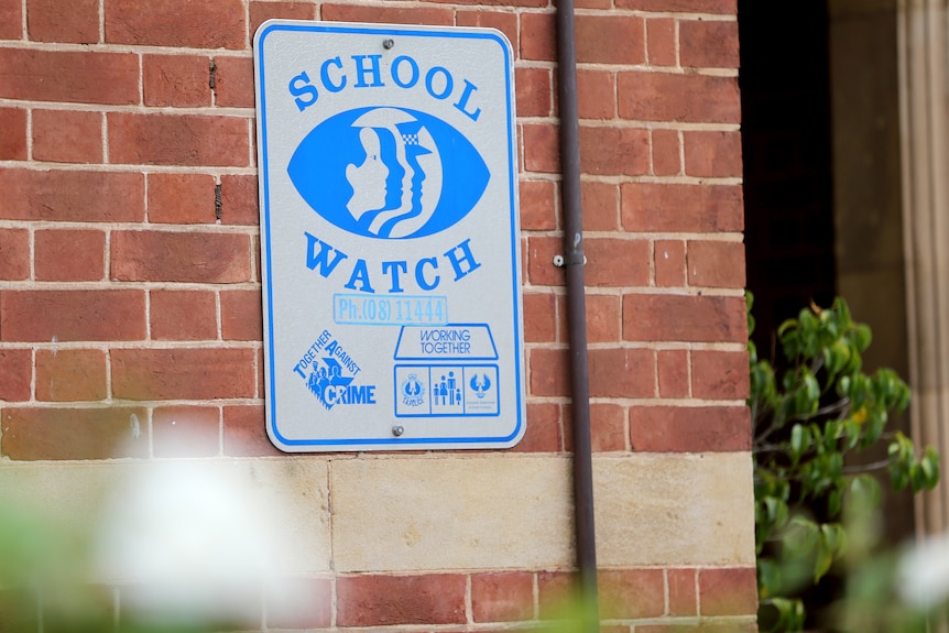 A sign showing a school watch on a brick wall.
