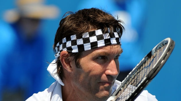 A close-up photograph of tennis player Pat Cash wearing a chequer headband and with a tennis racquet.