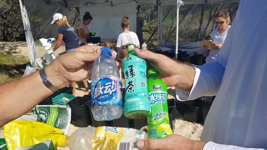 Volunteers holding plastic bottles with foreign labels found on Fraser Island