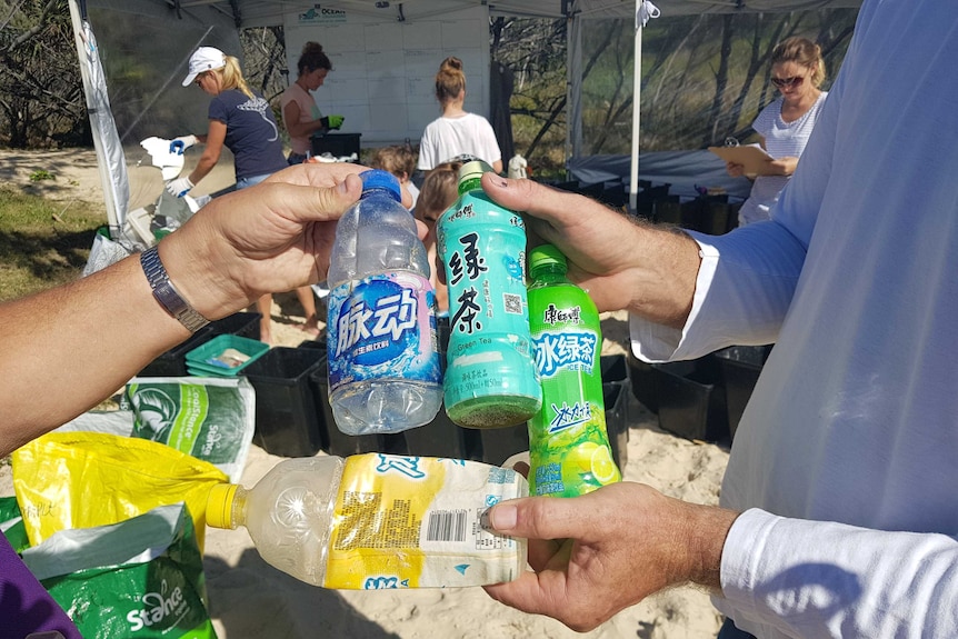 Volunteers holding plastic bottles with foreign labels found on Fraser Island
