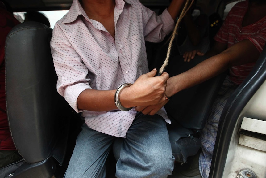 An unidentified man sits in a car and is restricted by handcuffs.