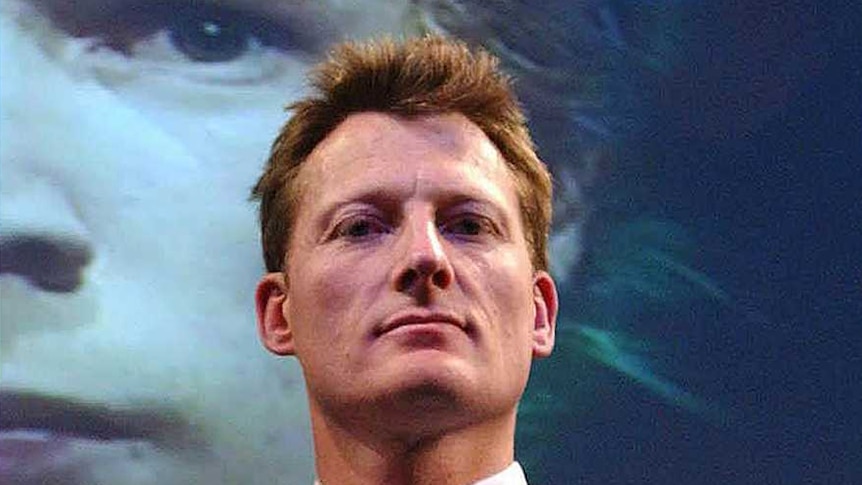 A man in a suit stands looking into the camera.