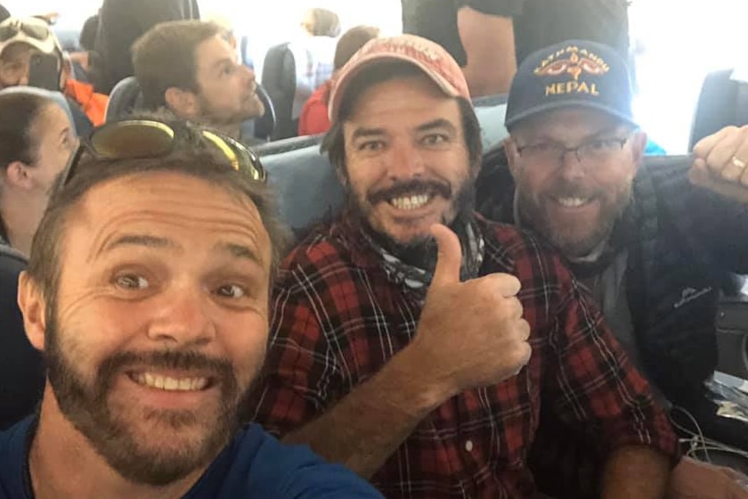 Three men give the thumbs up while sitting in plane chairs
