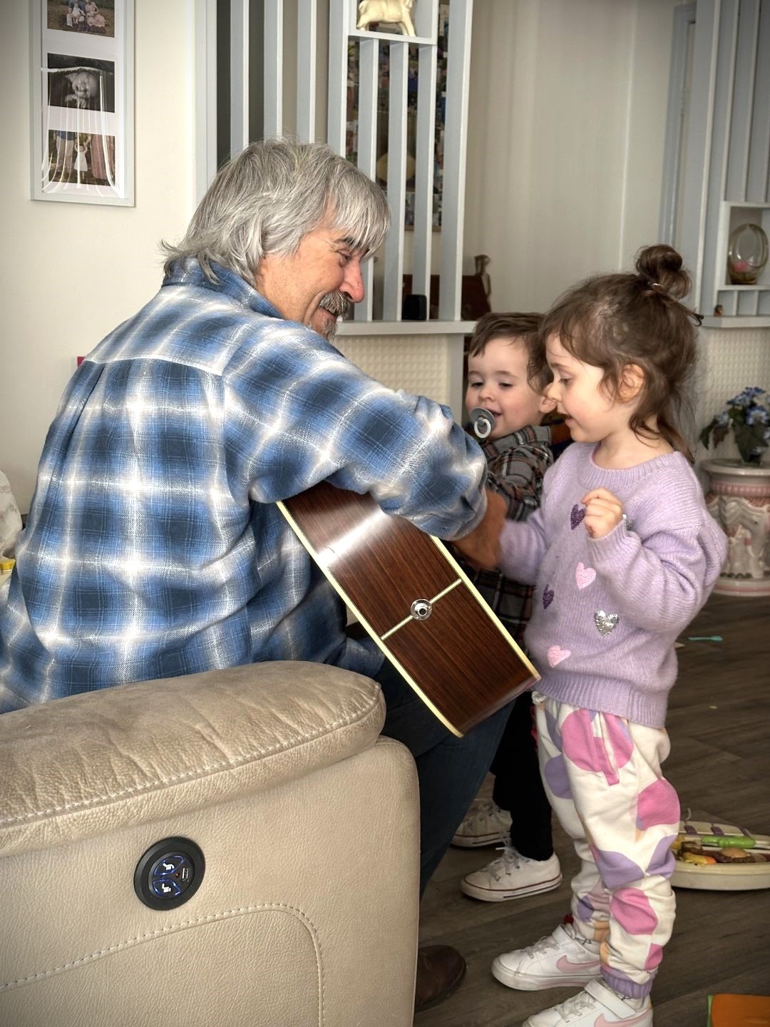 A man wearing a blue, black and white shirt playing the guitar to two young children