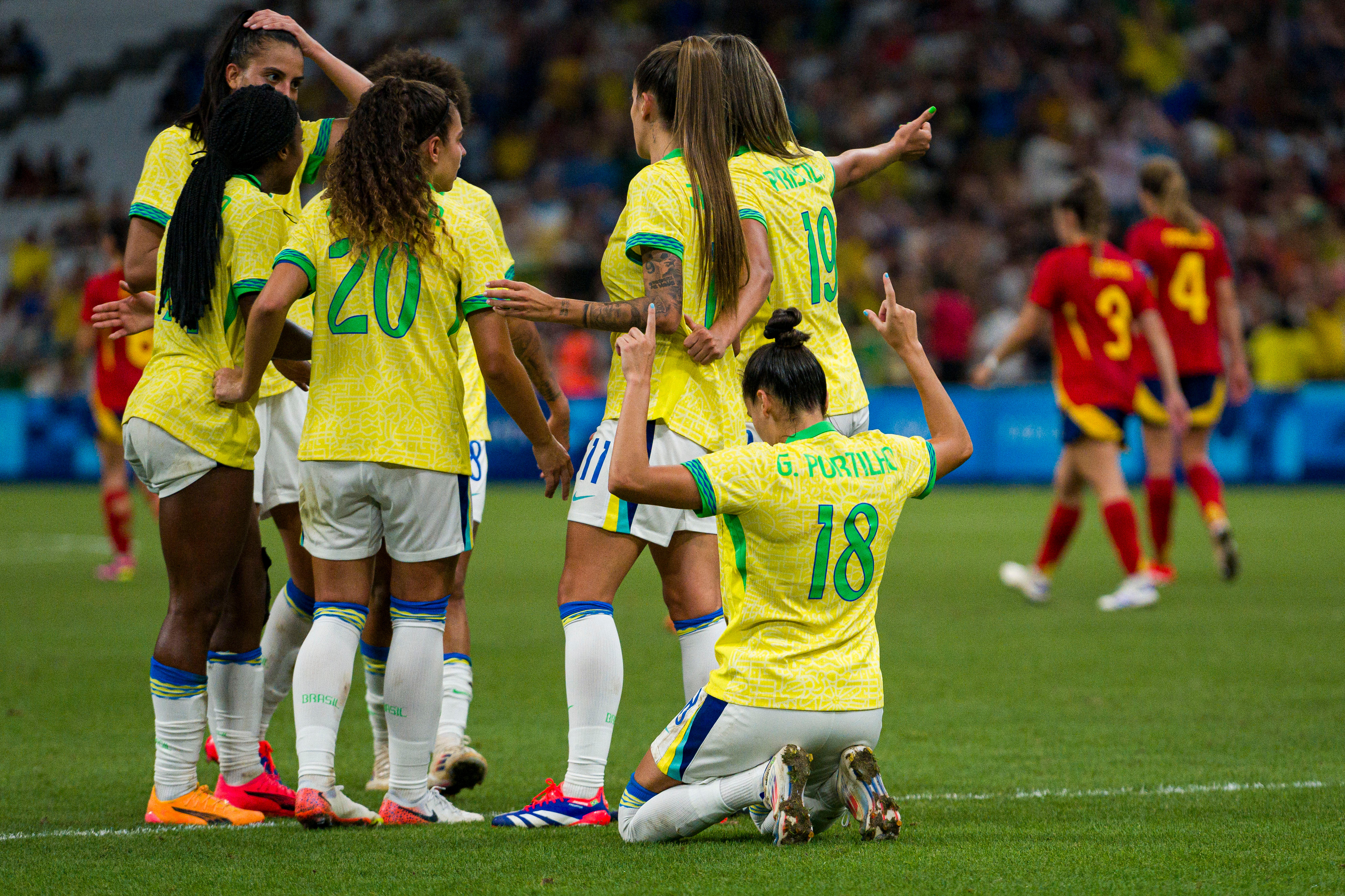 A women&#x27;s soccer team wearing yellow and white celebrate after scoring against a team in red and blue