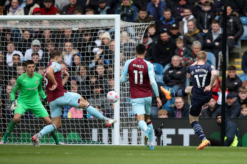 Manchester City's Kevin de Bruyne extends his foot as the ball sails past defenders to the net as the goalkeeper watches.