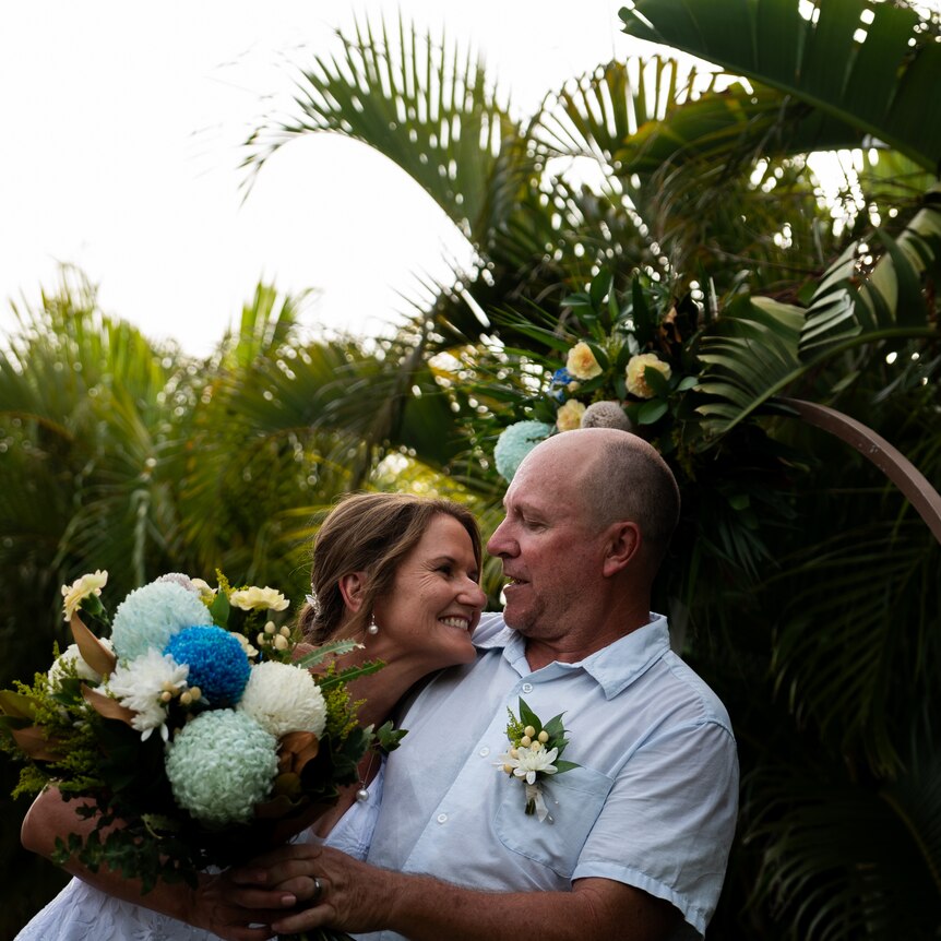 A man and a women embracing in front of palm trees on their wedding day