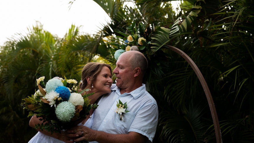 A man and a women embracing in front of palm trees on their wedding day