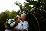A man and a women embracing in front of palm trees on their wedding day