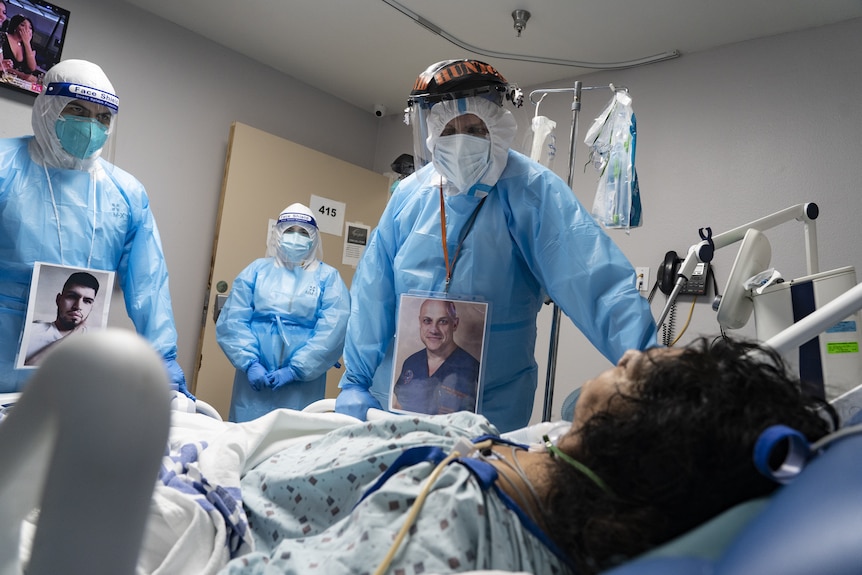 A group of medical professionals in protective wear and masks stand around an older person in an ICU clinic