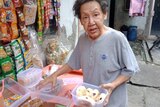 A trans woman with a box of cakes at a streetside vendor.